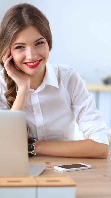 Attractive businesswoman sitting on desk in the office
